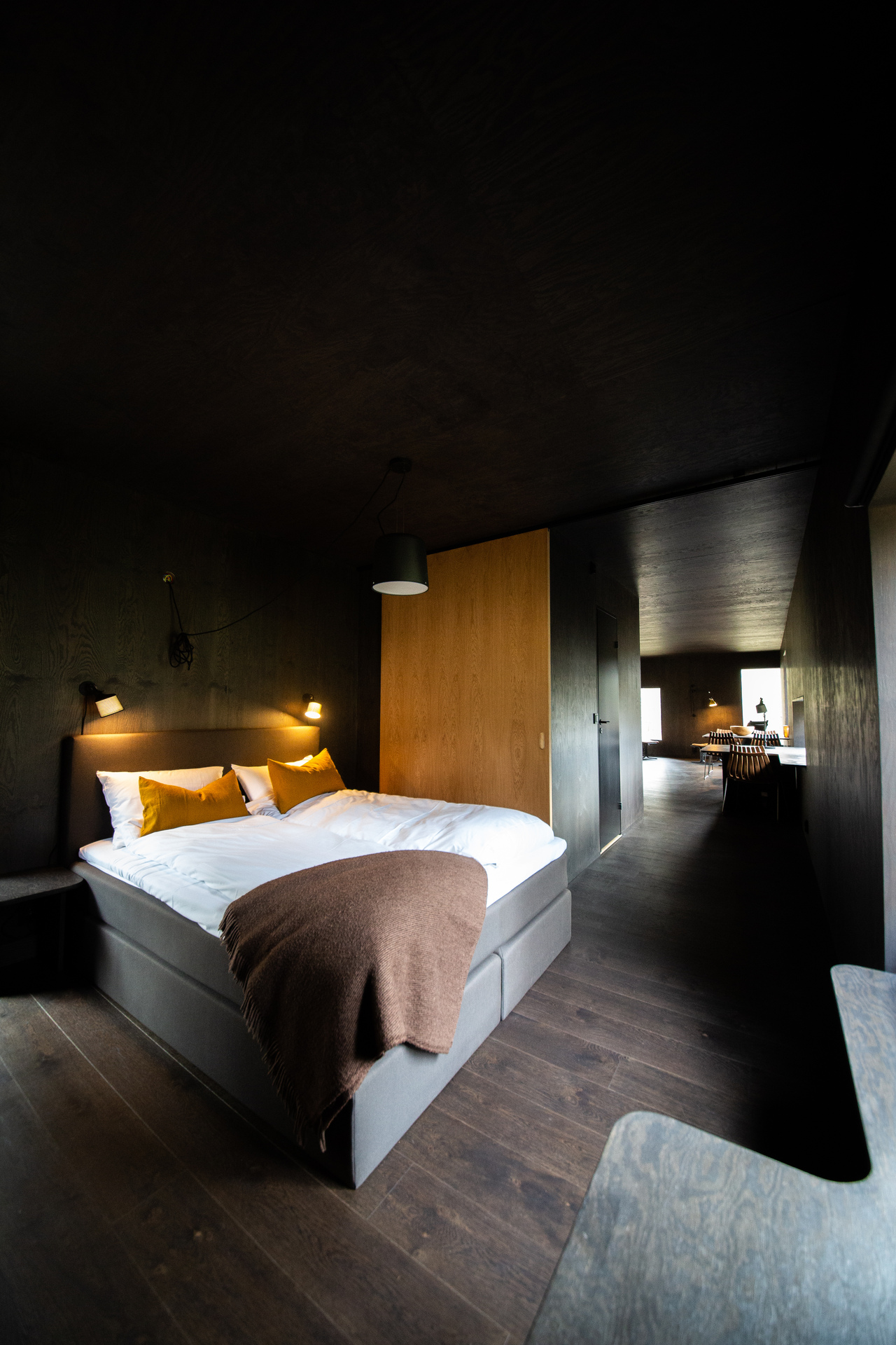 Hotellrom med mørke flater og stor seng.